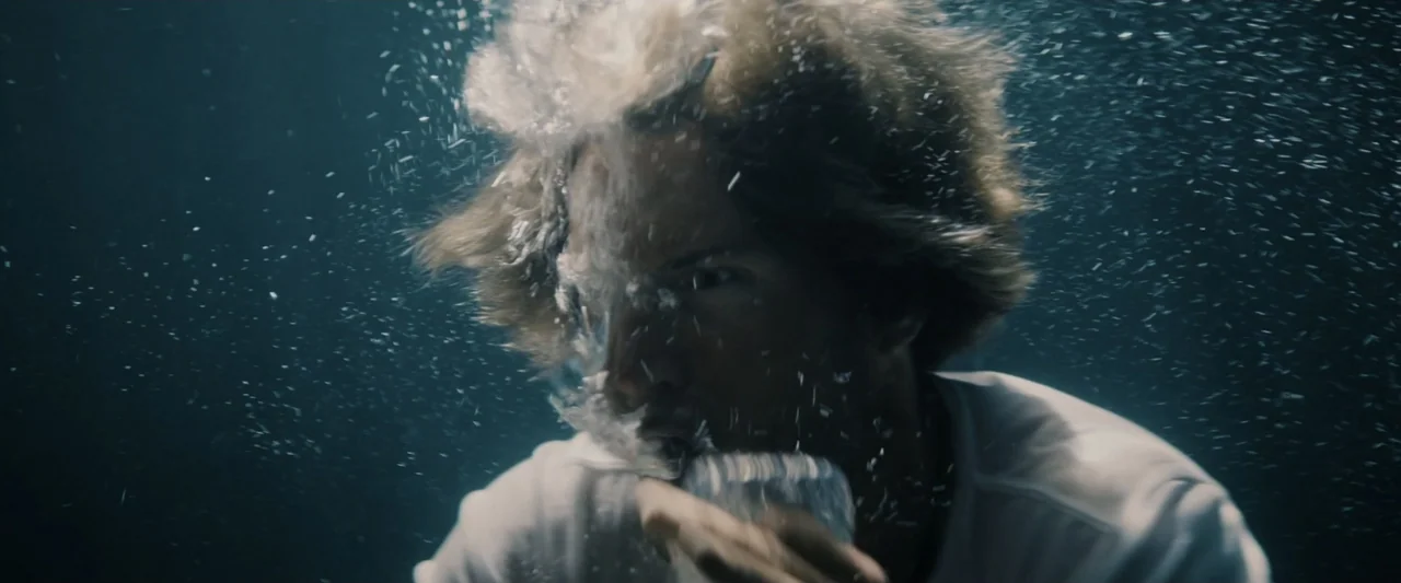 Great White (1998) movie still: closeup — A person is submerged deep underwater with turbulent air bubbles surrounding their head. They wear a white…