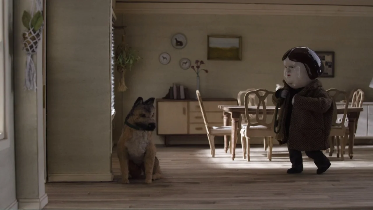 Bestia (2017) movie still: medium — A miniature dining room features a wooden table, chairs, and framed artwork on walls. A stylized figure in a…