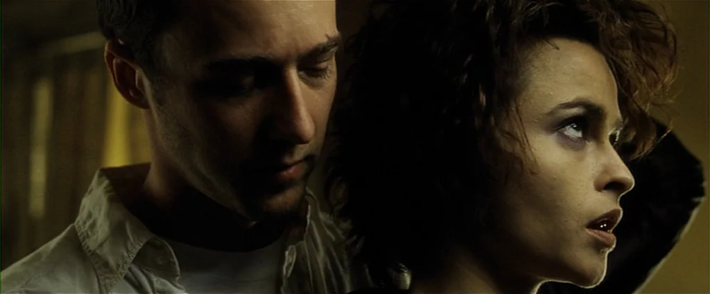 Fight Club (1999) movie still: closeup — A dark, dimly lit room with muted earth tones and deep, shadowy background textures. A man stands close to…