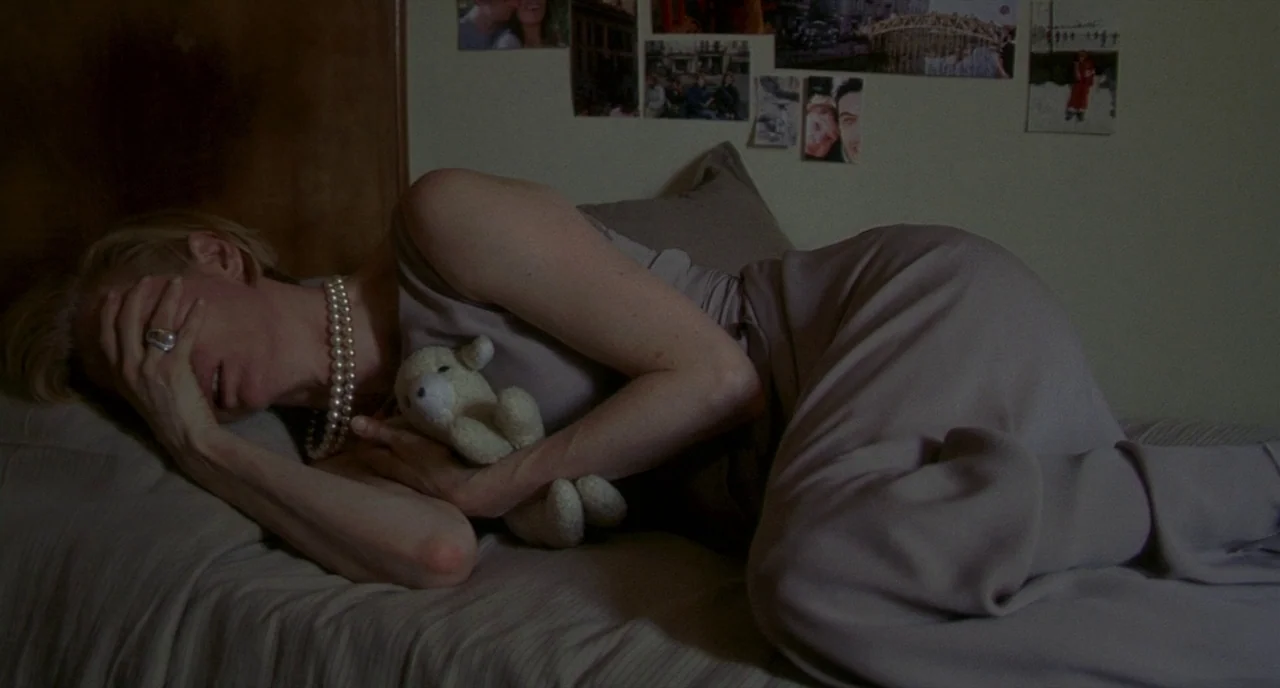 Making of: I Am Love (2009) movie still: medium — A dimly lit room with muted walls features several photographs taped above a bed. A blonde woman…