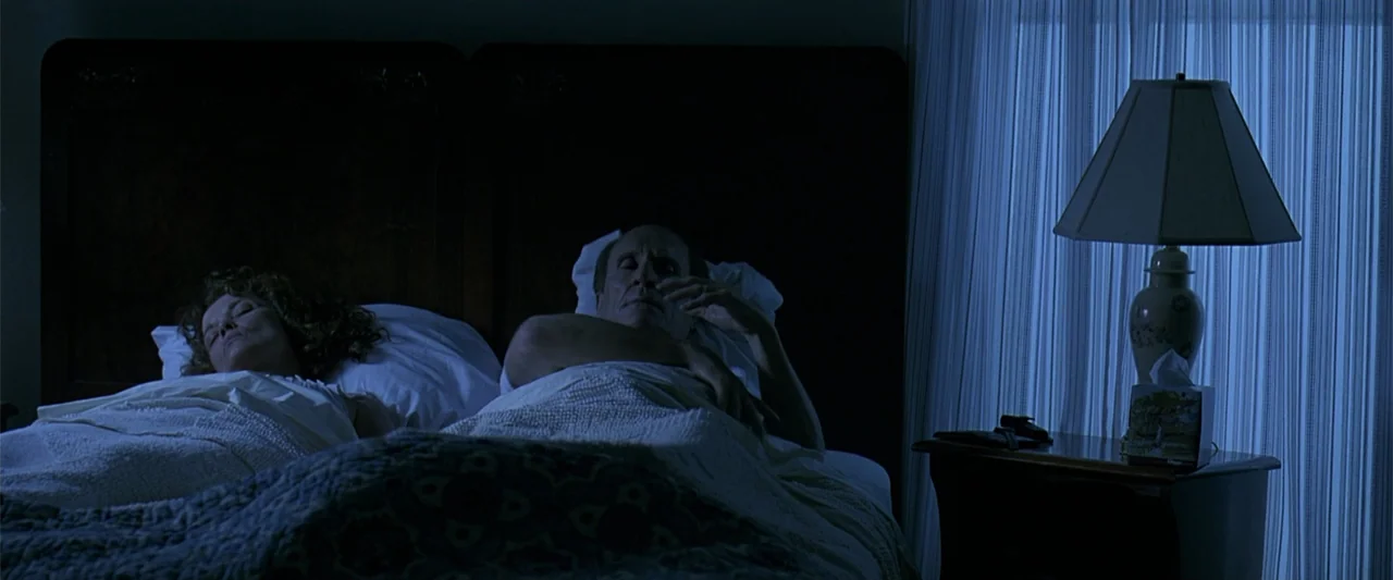 A Family Thing (1996) movie still: medium — A dimly lit bedroom at night with a table lamp on the right side. A couple rests in a large dark-framed…