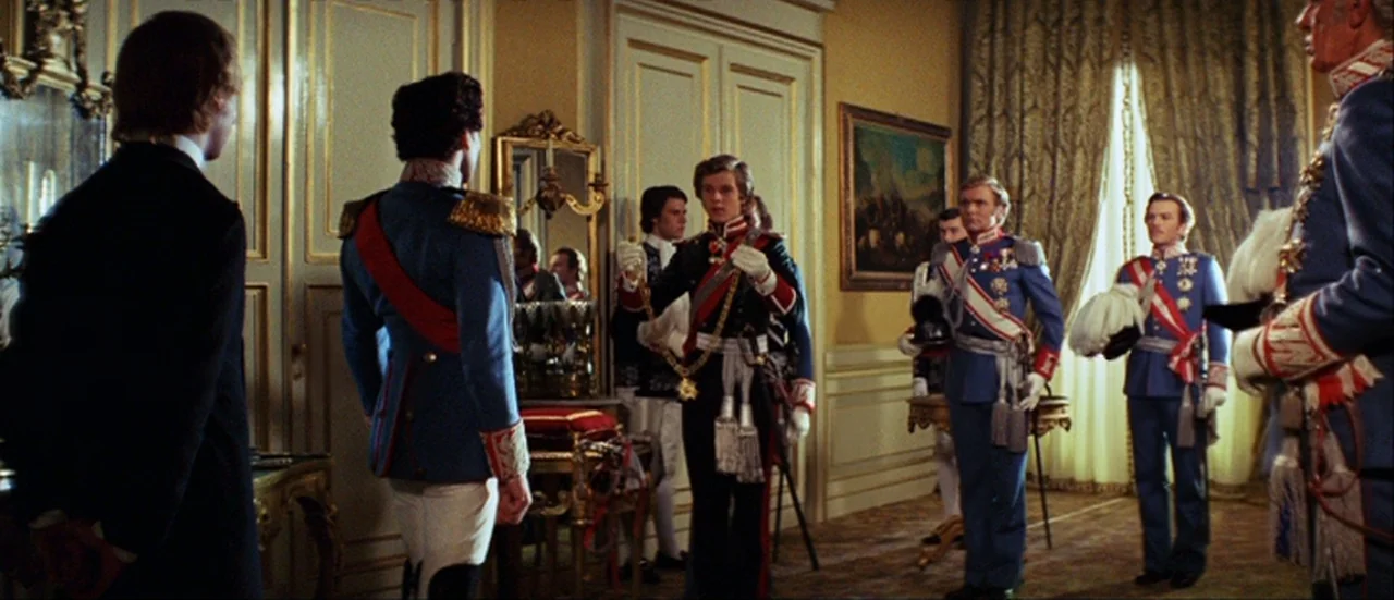 Ludwig (1973) movie still: wide — A grand reception hall featuring yellow walls and tall white paneled doors. Several men in colorful formal…