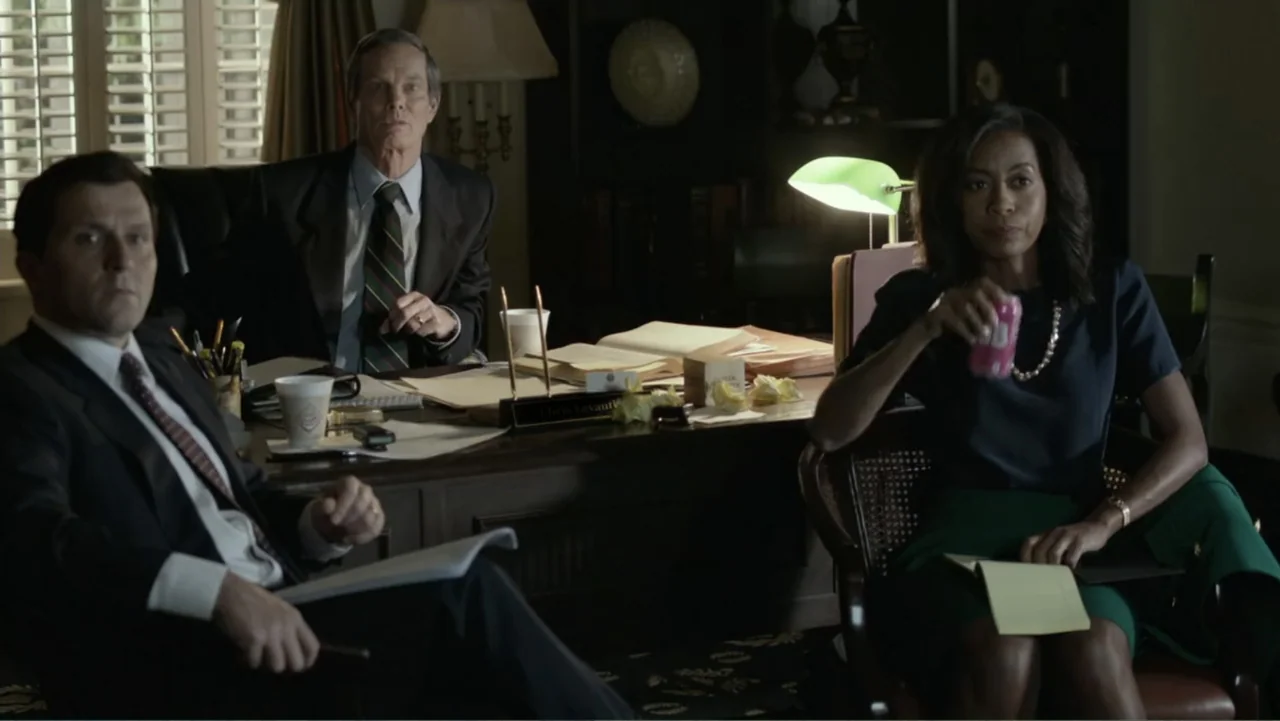 Confirmation (2016) movie still: medium — A wood-paneled professional office contains a dark desk with papers and a lamp. Three individuals in…