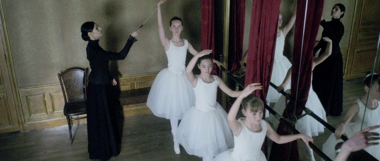 Livid (2011) movie still: medium — A historic dance studio features gold-toned walls and tall mirrors draped in red fabric. Three young ballerinas…