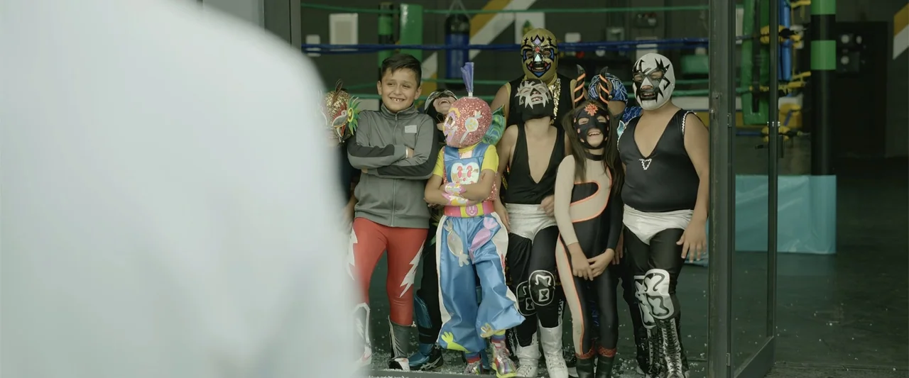 Divine Intervention (2026) movie still: medium — A group of children wearing luchador wrestling masks pose inside a training facility. The children…