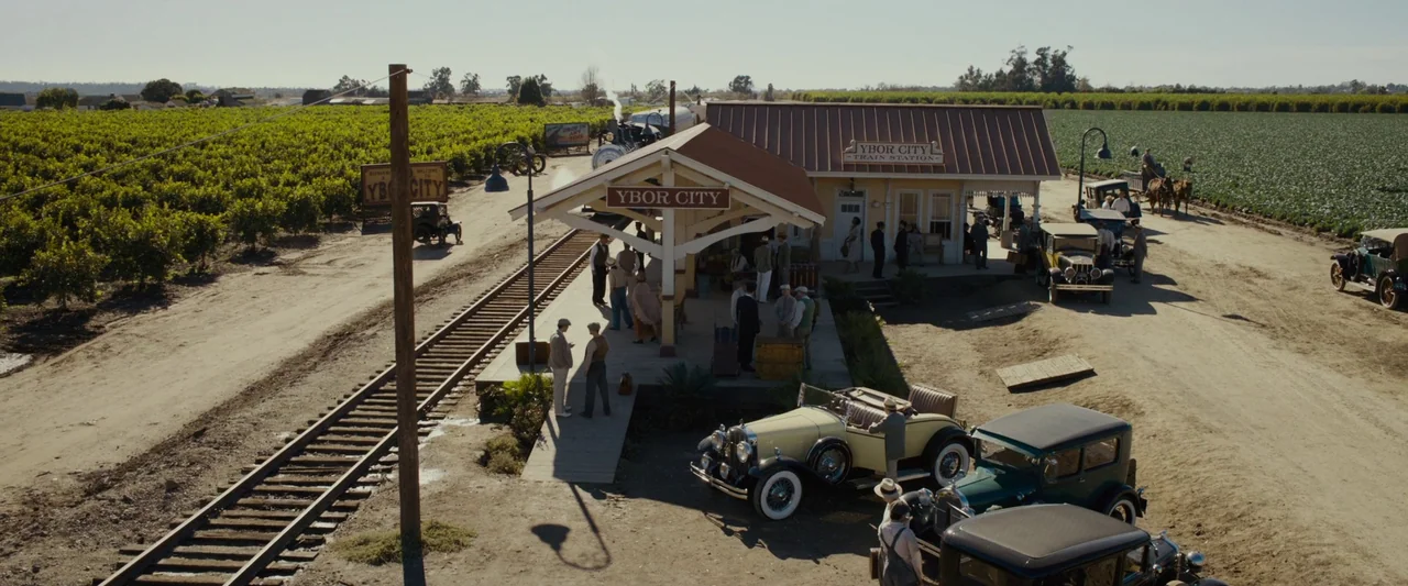 Live By Night (2016) movie still: establishing — A rural train station named Ybor City sits beside expansive green agricultural fields. Multiple…