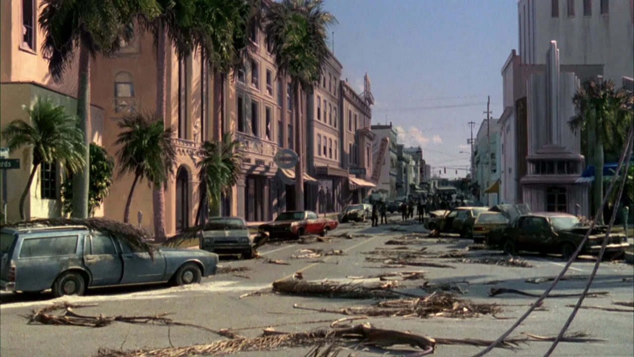 Day of the Dead (1985) movie still: establishing — A wide, debris-strewn urban avenue is lined with Art Deco style buildings and palm trees.…
