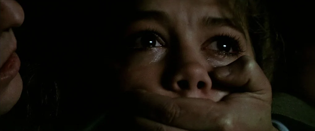Anguish (1987) movie still: closeup — A dark, undifferentiated interior space obscures all background details. A large hand covers the lower face of…