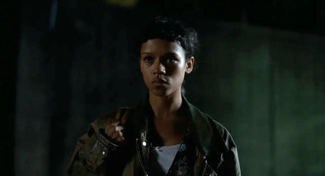 Bones and All (2022) movie still: medium — A woman stands in a dark and indistinct urban outdoor space at night. She is positioned against a shadowy…