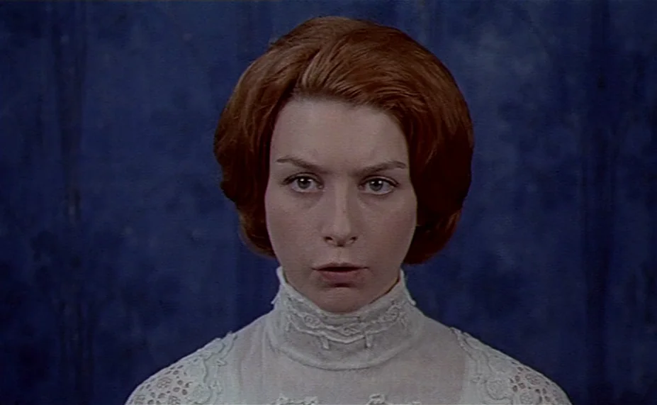 Two English Girls (1971) movie still: closeup — A woman stands before a dark blue, textured wall surface. She stares directly ahead at the camera.