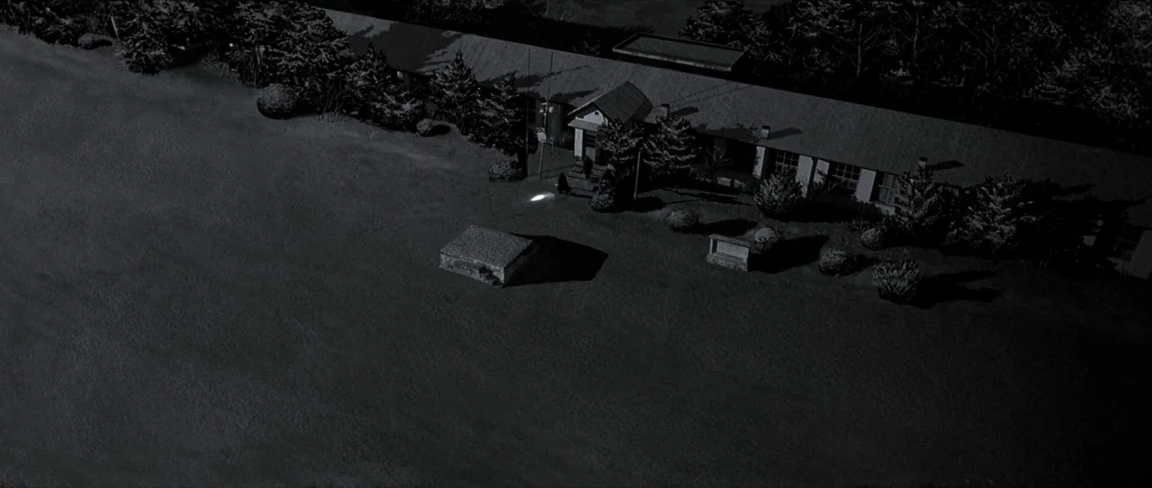 Lady Vengeance (2005) movie still: establishing — A nighttime aerial view shows a school building adjacent to a large dark lawn. A single glowing…