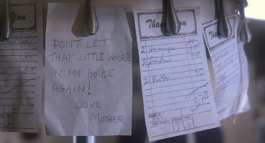 Psycho 2 (1983) movie still: closeup — A series of white paper order tickets are secured to a metal spinning rack. One handwritten note on a ticket…