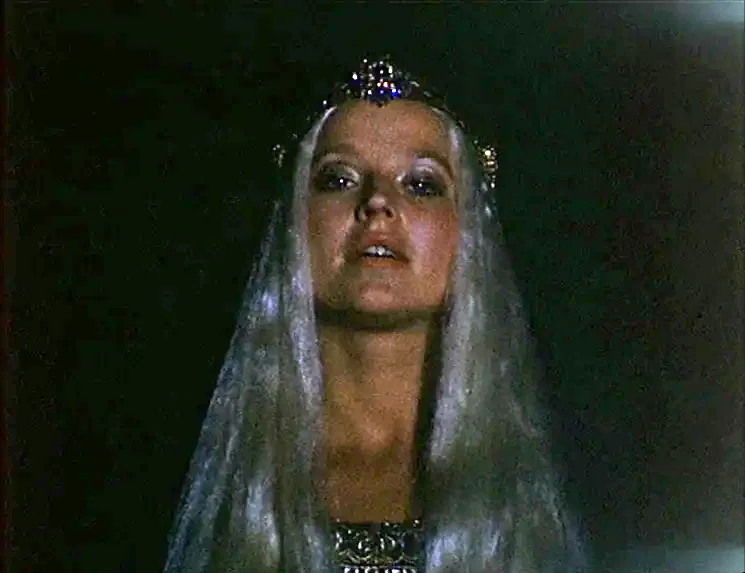 The Niklashausen Journey (1970) movie still: closeup — A dark space serves as the backdrop for a female figure. The woman wears a jeweled tiara and…
