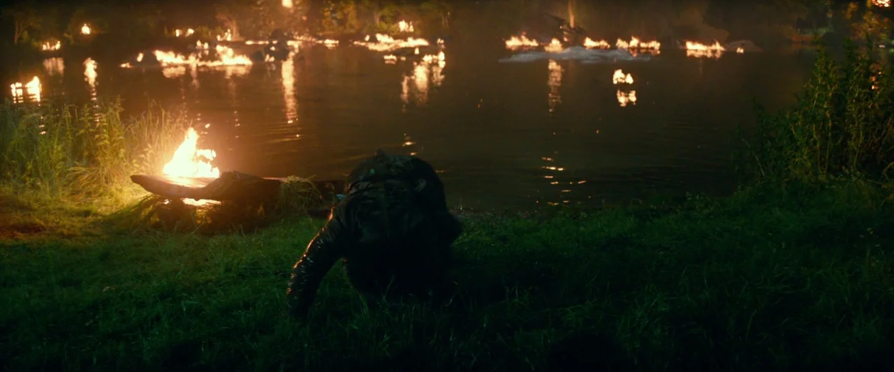 Overlord (2018) movie still: wide — A dark grassy bank meets a lake illuminated by multiple fires along the opposite shore. A single person in a…