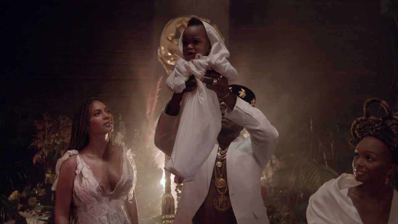 Black is King (2020) movie still: medium — A dimly lit ceremonial space filled with smoke and blurred organic elements. A man in a white suit lifts…