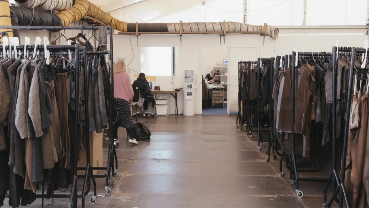 Game of Thrones: The Last Watch (2019) movie still: wide — A spacious costume storage facility features long rows of rolling garment racks and…