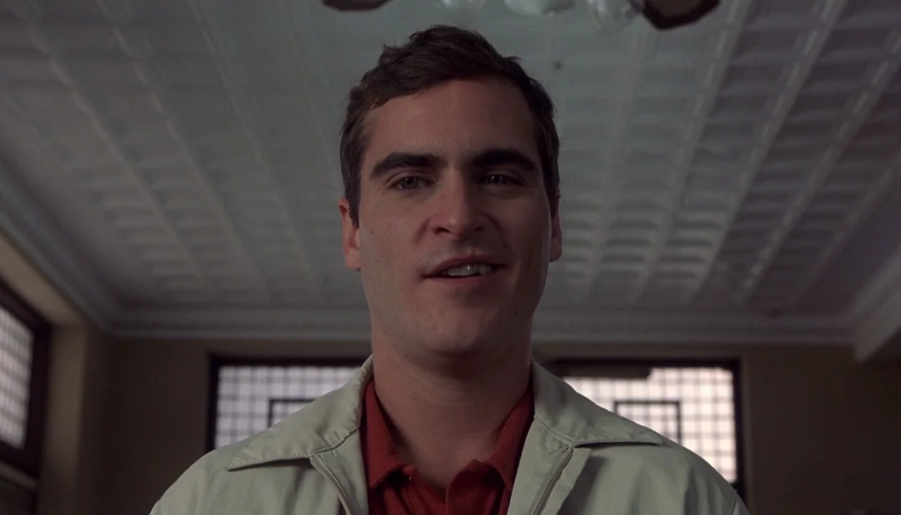 Signs (2002) movie still: closeup — A room with a white tin ceiling and grid-patterned windows in the background. A young man looks toward the…