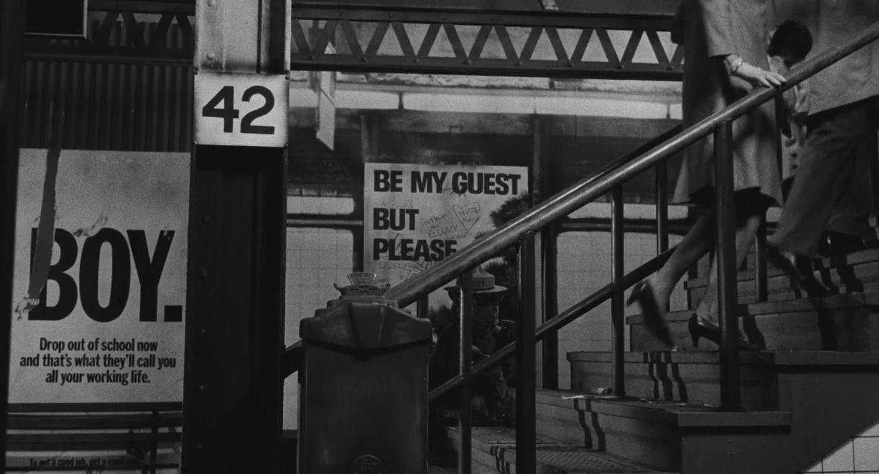 The Incident (1967) movie still: wide — A tiled subway stairwell features printed posters on the walls with numerical signage. Two blurred…