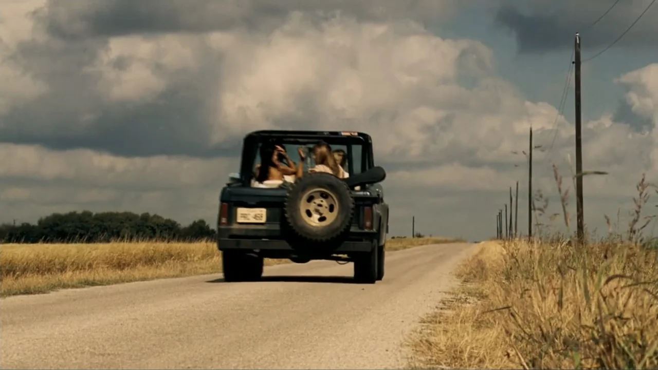 The Texas Chainsaw Massacre: The Beginning (2006) movie still: wide — A dark off-road vehicle drives down a long, narrow paved rural road. The road…