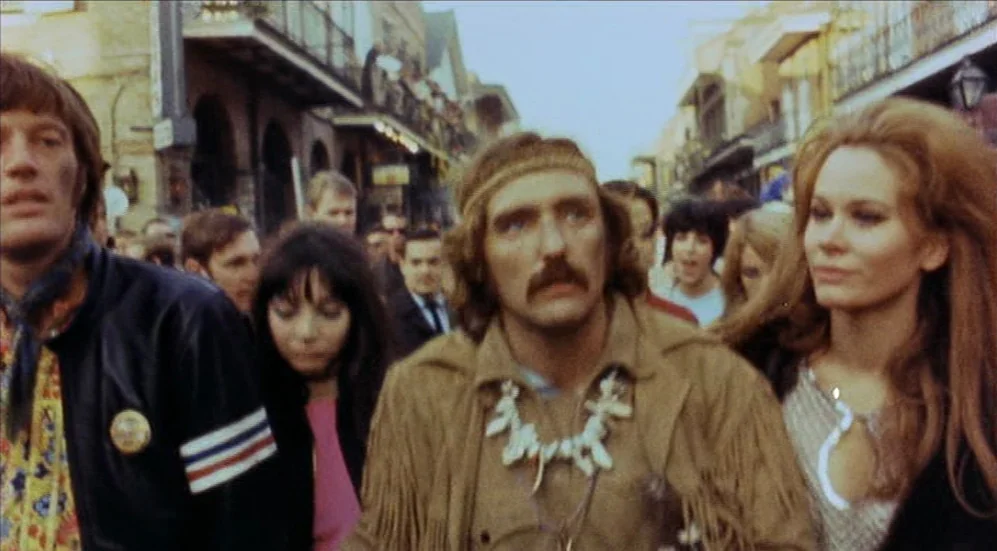 Easy Rider (1969) movie still: medium — A crowded city street features historic architecture with iron-wrought balconies overhead. A small group of…