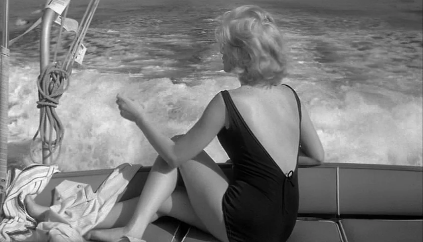 L’Avventura (1960) movie still: medium — The back of a moving boat shows a wake in the water behind it. A woman in a black swimsuit sits on the boat…
