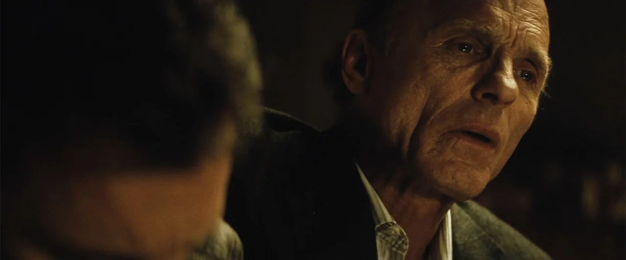 Run All Night (2015) movie still: closeup — A dark indoor space with minimal visibility of the background environment. An elderly man in a dark…