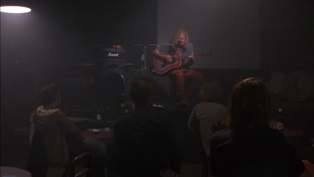 Before Sunrise (1995) movie still: wide — A dimly lit club with a small stage and several patrons watching a performance. A long-haired man sits on…