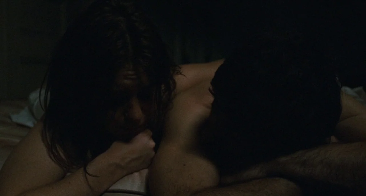 The Panic in Needle Park (1971) movie still: medium — A dark, dimly lit space with a couple lying in bed together. They are reclined on white…