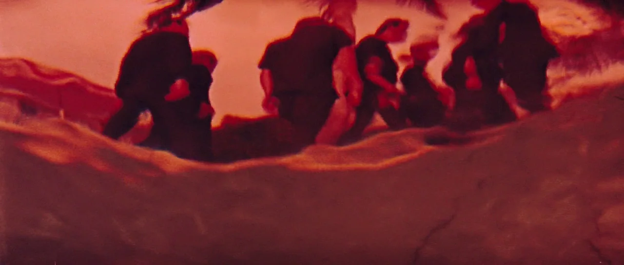 Thunderball (1965) movie still: wide — A group of people walk away across sand under a bright, reddish sky. Their dark figures appear as silhouettes…