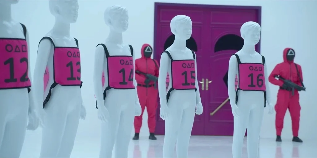 Making of: Squid Game (2021) movie still: medium — A sterile white room features a vibrant magenta door centered in the back wall. Five white…