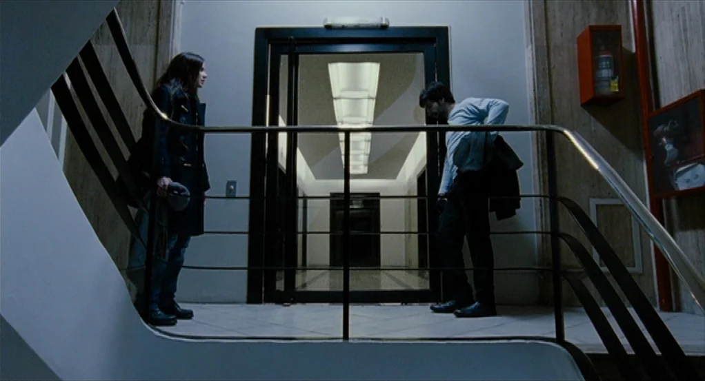 Sidewalls (2011) movie still: fullbody — A sterile stairwell landing features marble-patterned walls and a bright glass doorway entrance. A man and…