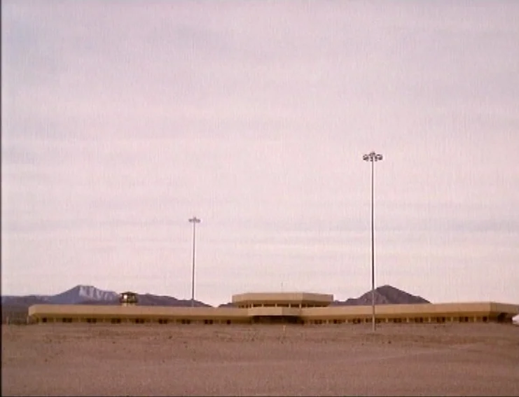 Ghosts… Of The Civil Dead (1988) movie still: establishing — A sprawling prison facility sits in an empty, arid desert landscape under overcast…