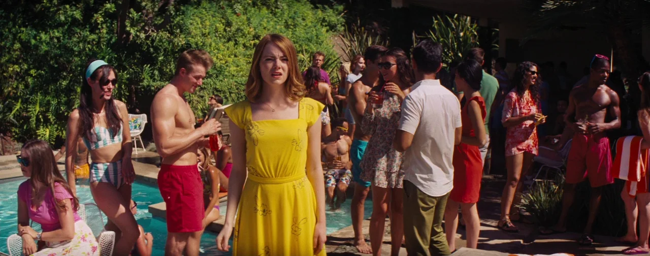 La La Land (2016) movie still: medium — A sunny outdoor pool party features a crowd of people in vibrant summer attire. A young woman in a yellow…