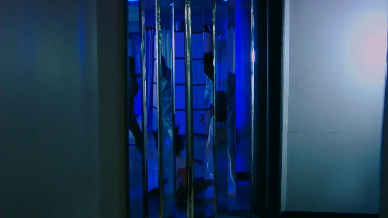 Merantau (2009) movie still: medium — A narrow corridor features a series of vertical mirror panels reflecting a blue-lit space. A figure stands…