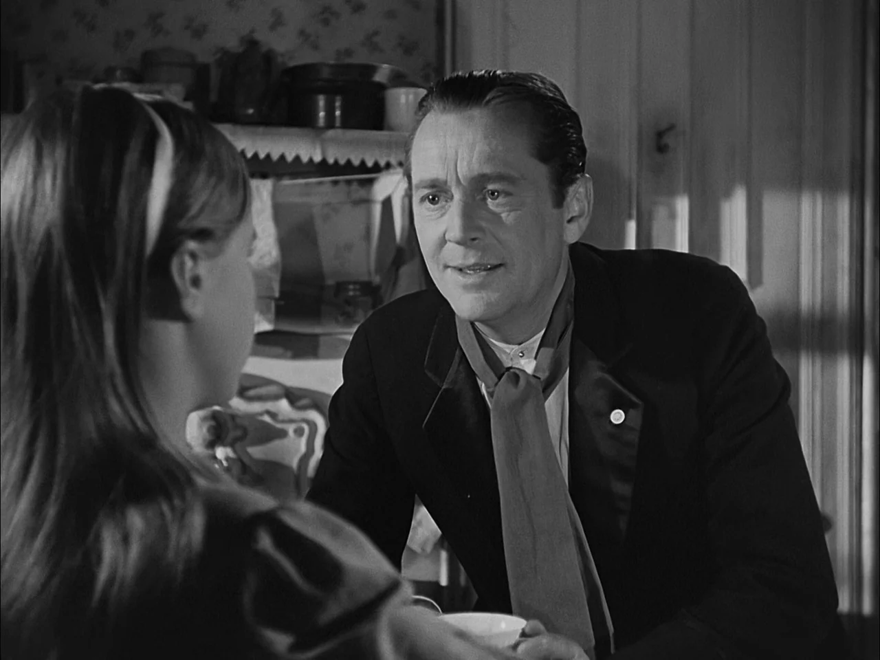 A Tree Grows In Brooklyn (1945) movie still: medium — A rustic interior with wooden walls and patterned wallpaper featuring a dark shelf unit. A man…