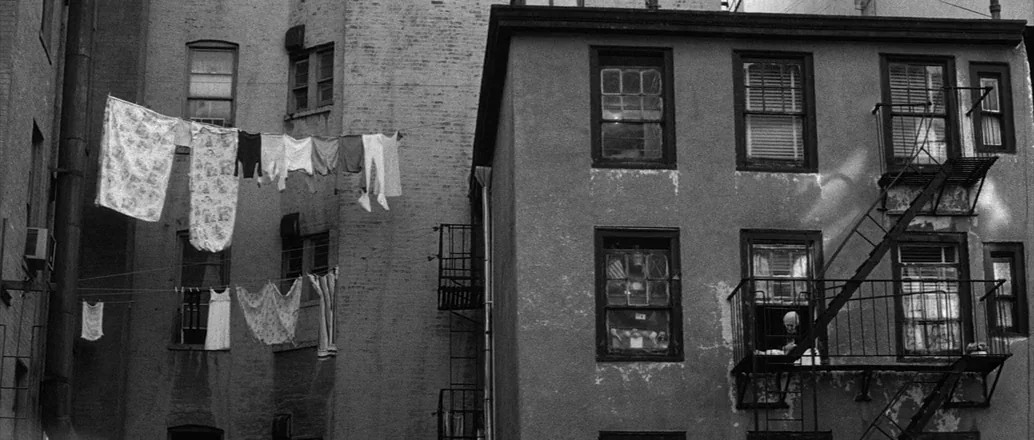 Manhattan (1979) movie still: wide — A dense urban courtyard is enclosed by weathered brick tenement buildings with fire escapes. Multiple lines of…