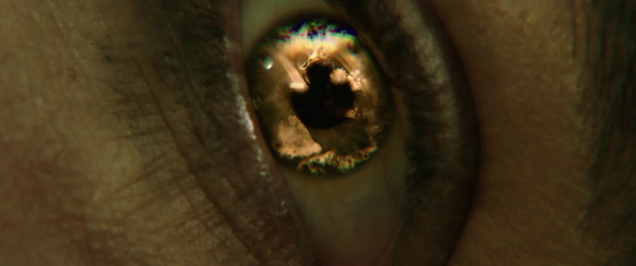 Happy Death Day (2017) movie still: closeup — An extreme close-up view of a human eye focused on the iris detail. A bright light source is reflected…