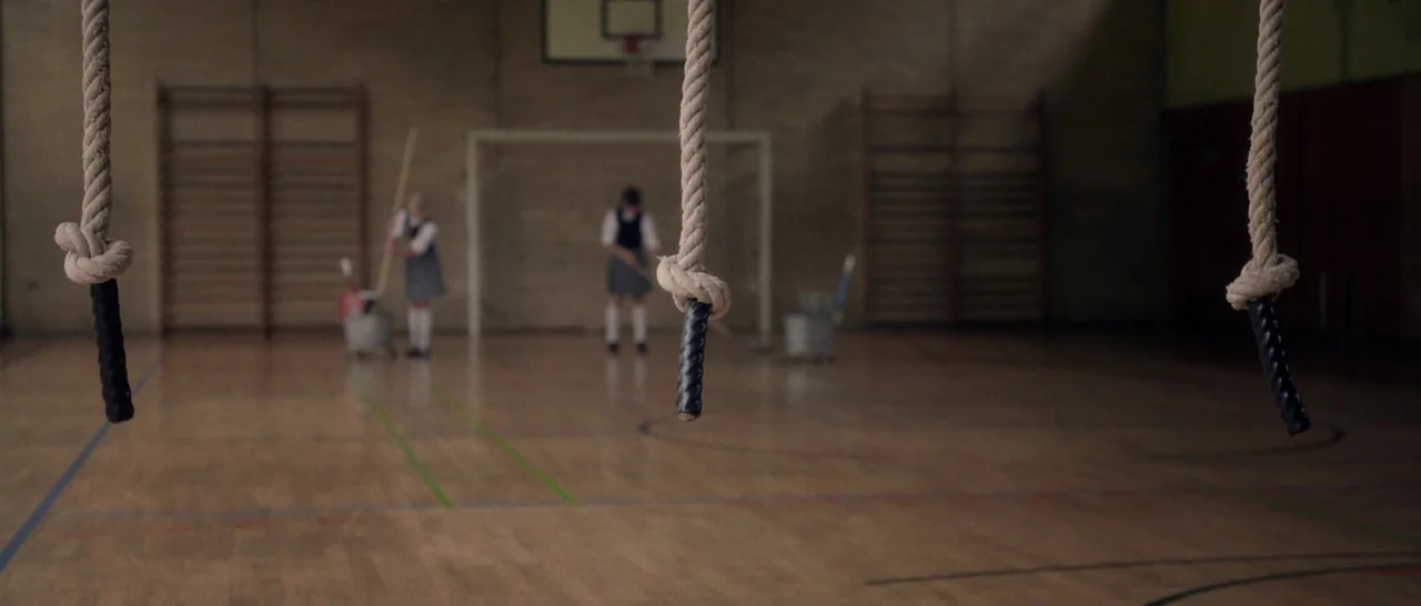 Nymphomaniac Vol 1 (2013) movie still: wide — A wooden floored school gymnasium features wall-mounted climbing frames and a basketball hoop. Two…