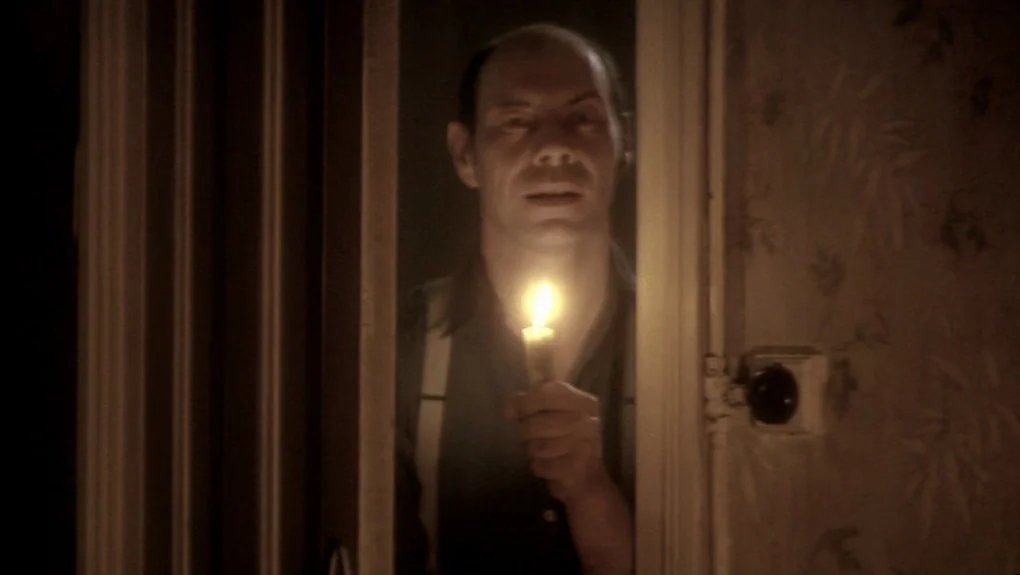 Distant Voices, Still Lives (1988) movie still: medium — A man stands within a narrow, dark doorway illuminated only by a small candle. The…