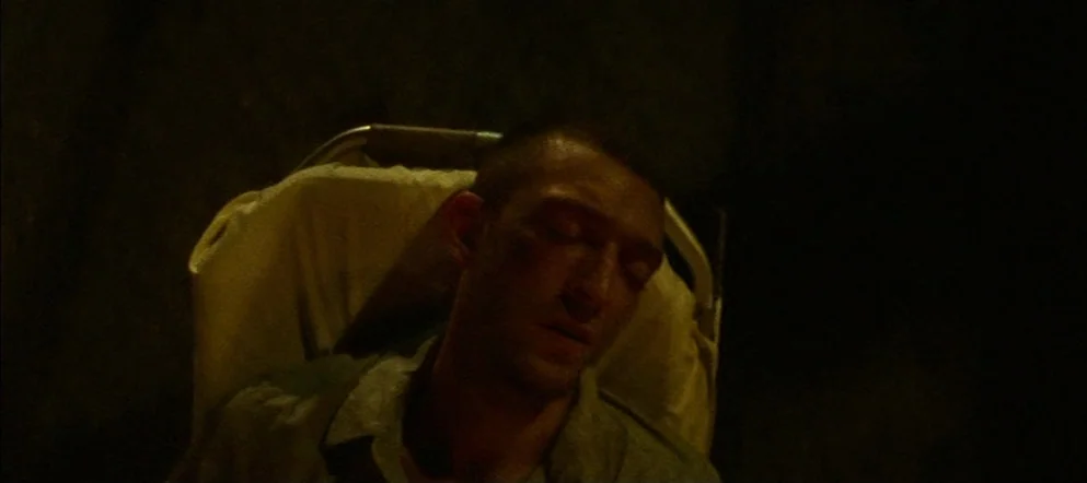 Irréversible (2002) movie still: medium — A man lies on a hospital bed within a dimly lit, dark room. He rests with his eyes closed while positioned…