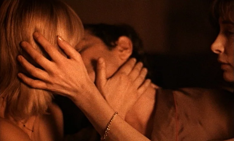 The Man Who Loved Women (1977) movie still: closeup — A dark bedroom lit by a warm, concentrated light source. Two individuals embrace and kiss with…