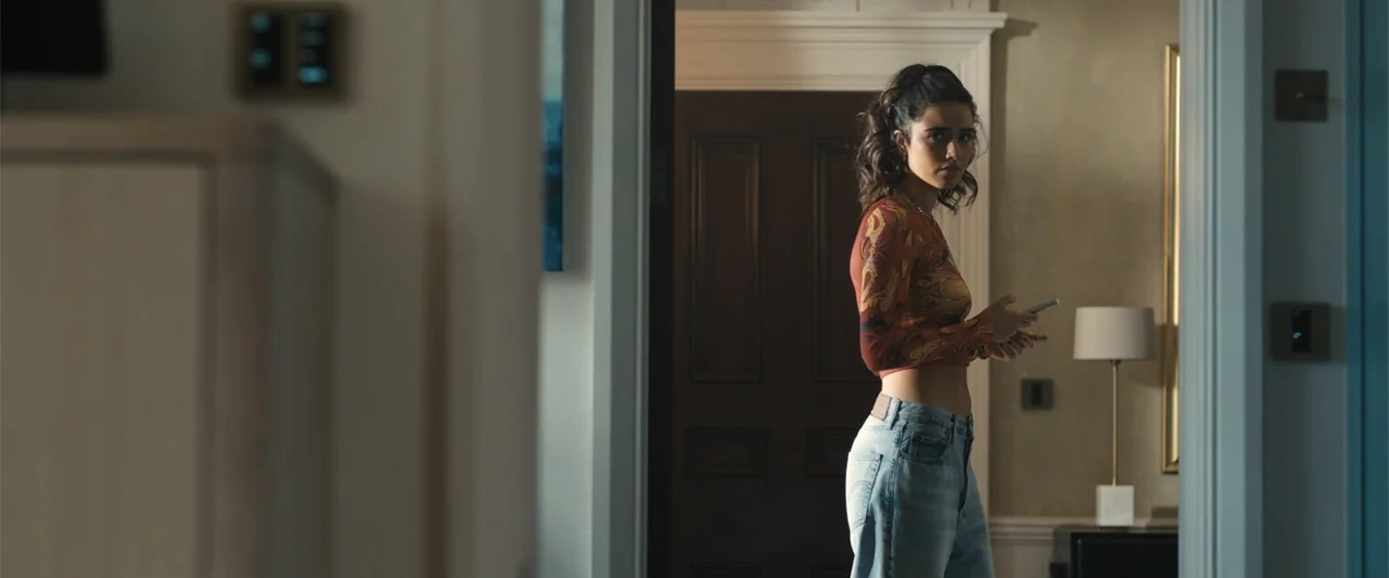 My Fault: London (2025) movie still: medium — A modern domestic hallway features light-colored walls and a dark wooden door frame. A young woman…