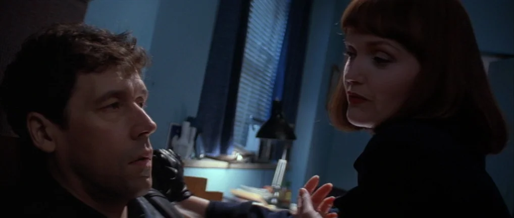 The Crying Game (1992) movie still: medium — A dimly lit room with a window covered by vertical blinds at night. A woman in a dark blazer speaks to…
