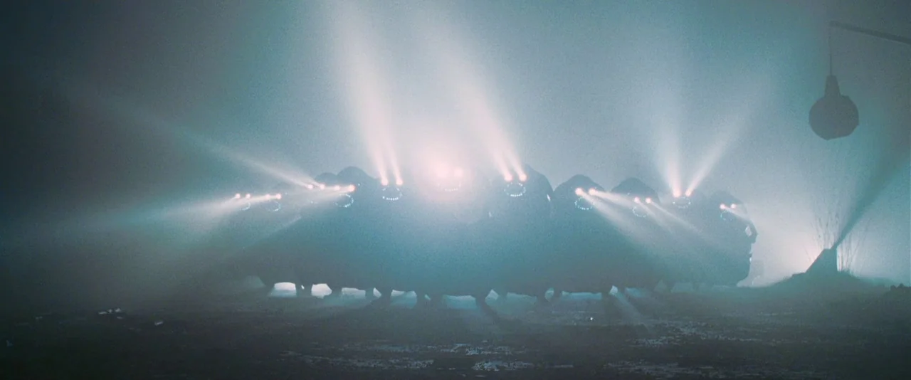 A Hitchhiker’s Guide To The Galaxy (2005) movie still: wide — A dark, mist-covered field contains a line of bulky, silhouetted creatures. Multiple…
