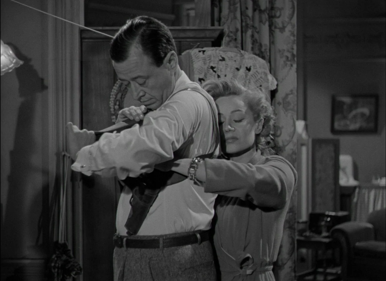 On Dangerous Ground (1951) movie still: medium — A furnished interior space with a patterned curtain and framed artwork on the wall. A woman stands…
