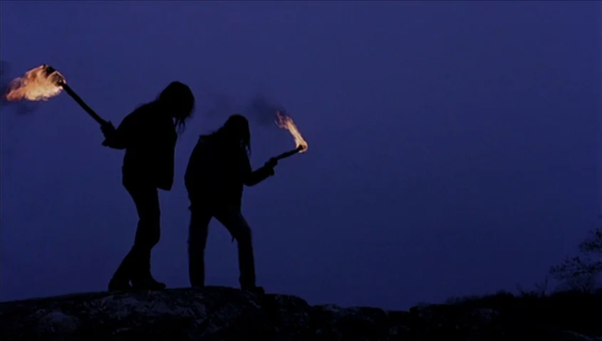 Dance Me Outside (1994) movie still: wide — Two individuals stand atop a dark, rocky ridge against a deep blue night sky. Both people hold lit…