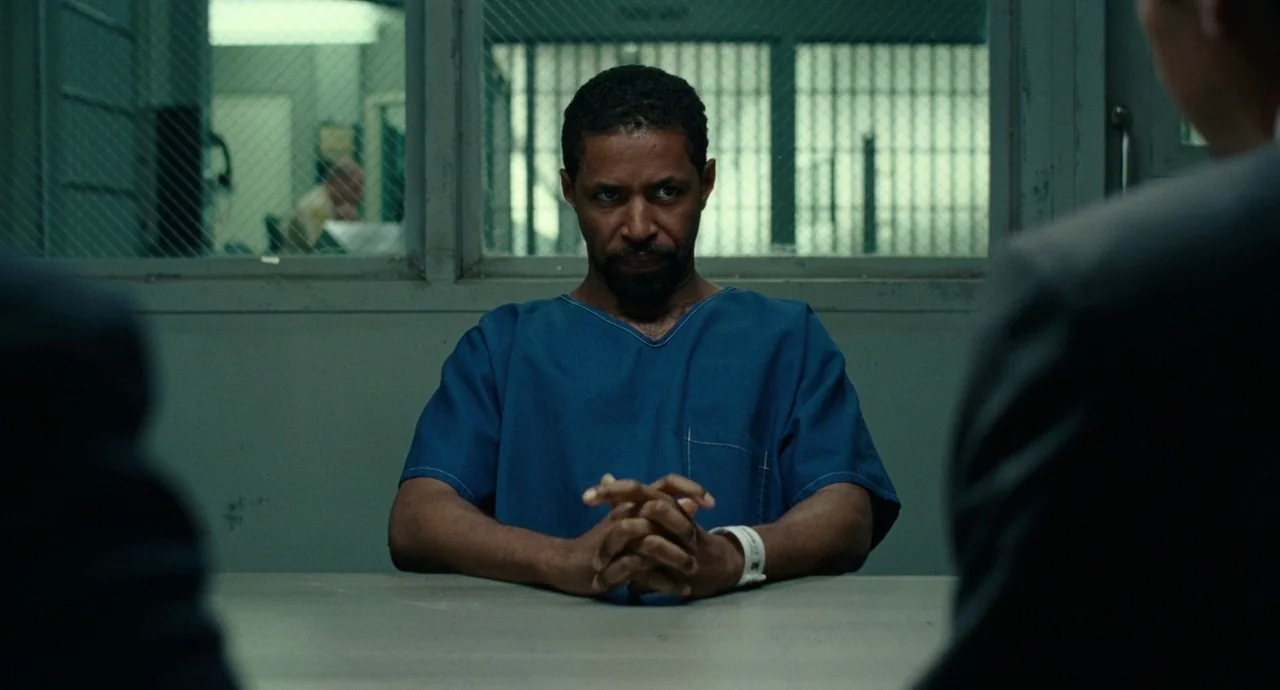 Roman J. Israel, Esq. (2017) movie still: medium — An interrogation room with a metal table and a wired glass window background. A man in blue…