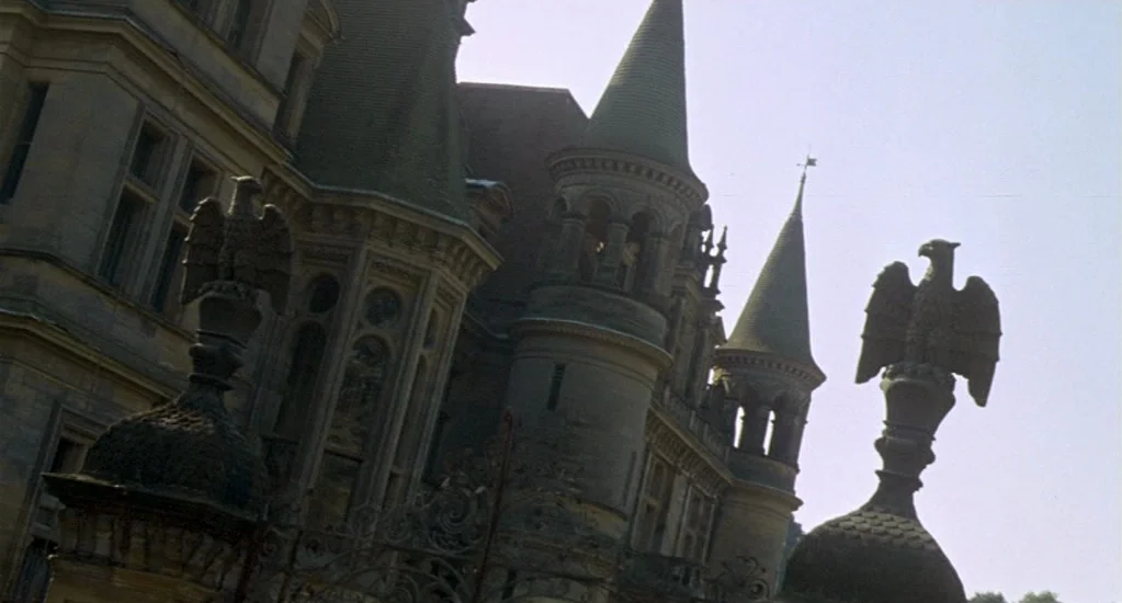 Demons of the Mind (1972) movie still: establishing — A stone mansion features multiple conical towers and ornate architectural details. Two eagle…