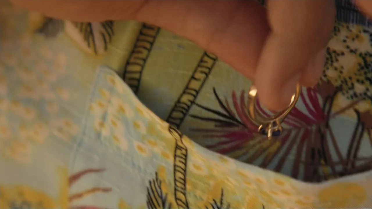 Double Pregnant 2 (2022) movie still: closeup — A close-up view shows a hand holding a ring against a tropical-patterned shirt. The fabric features…