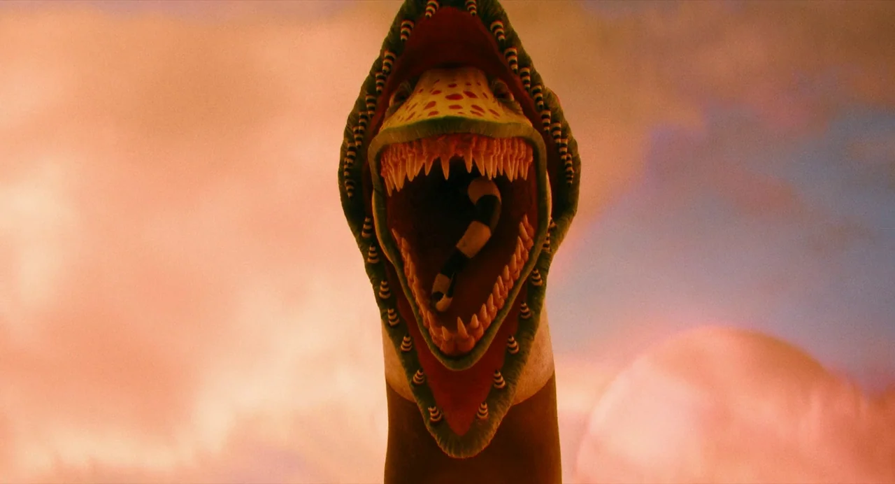 Beetlejuice Beetlejuice (2024) movie still: closeup — A giant serpentine creature stands against a vast, hazy orange-pink desert sky. The creature…